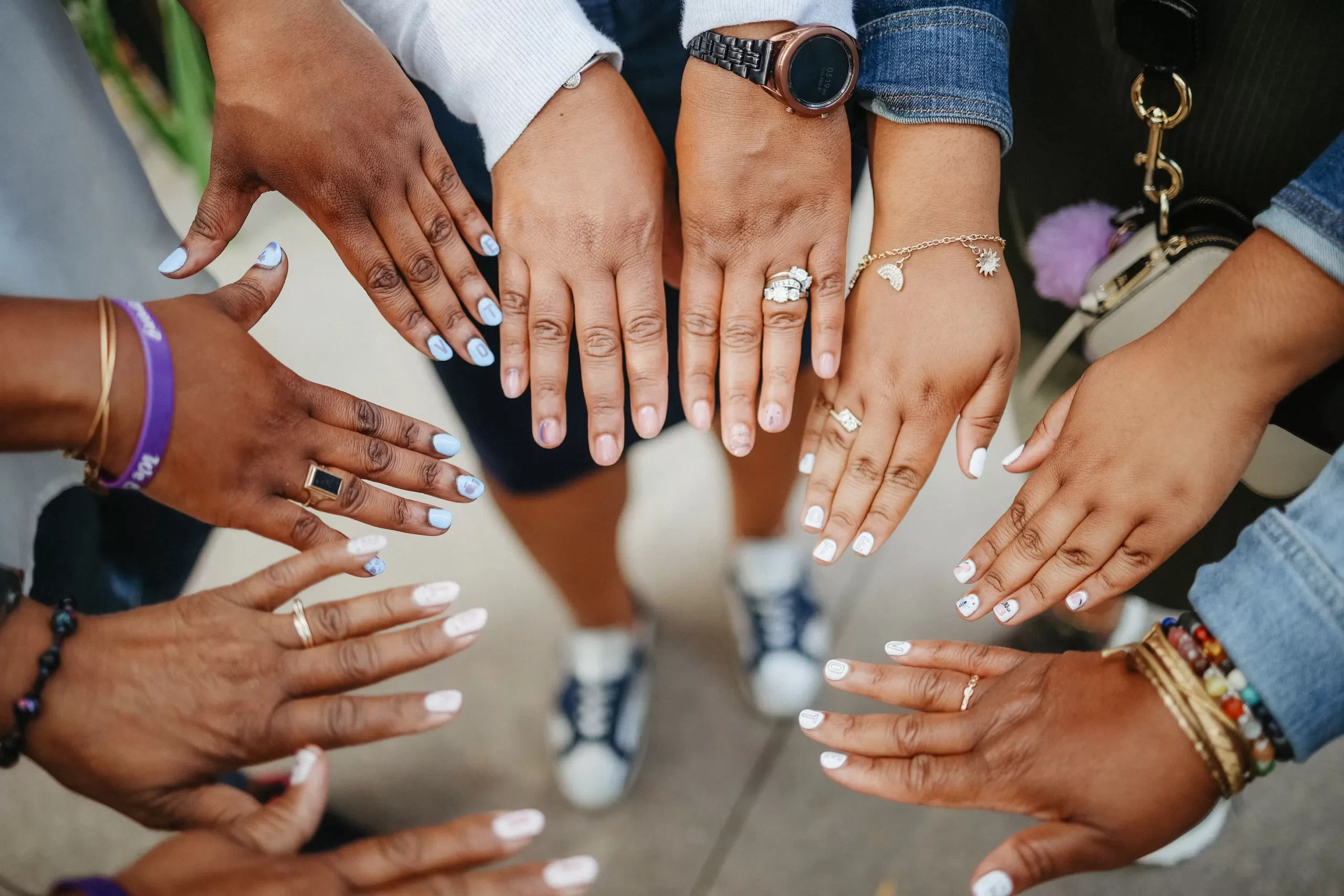 community-1 A group of people showing off manicured hands with various rings and bracelets arranged in a circle.