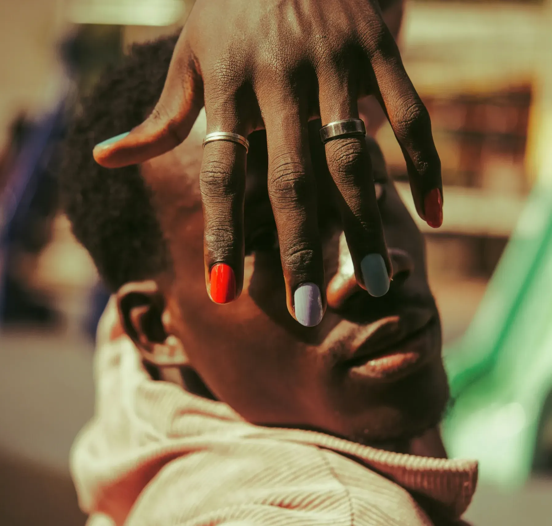 _nail-polish-4 A person with colorful nail polish and rings covers part of their face with their hand.